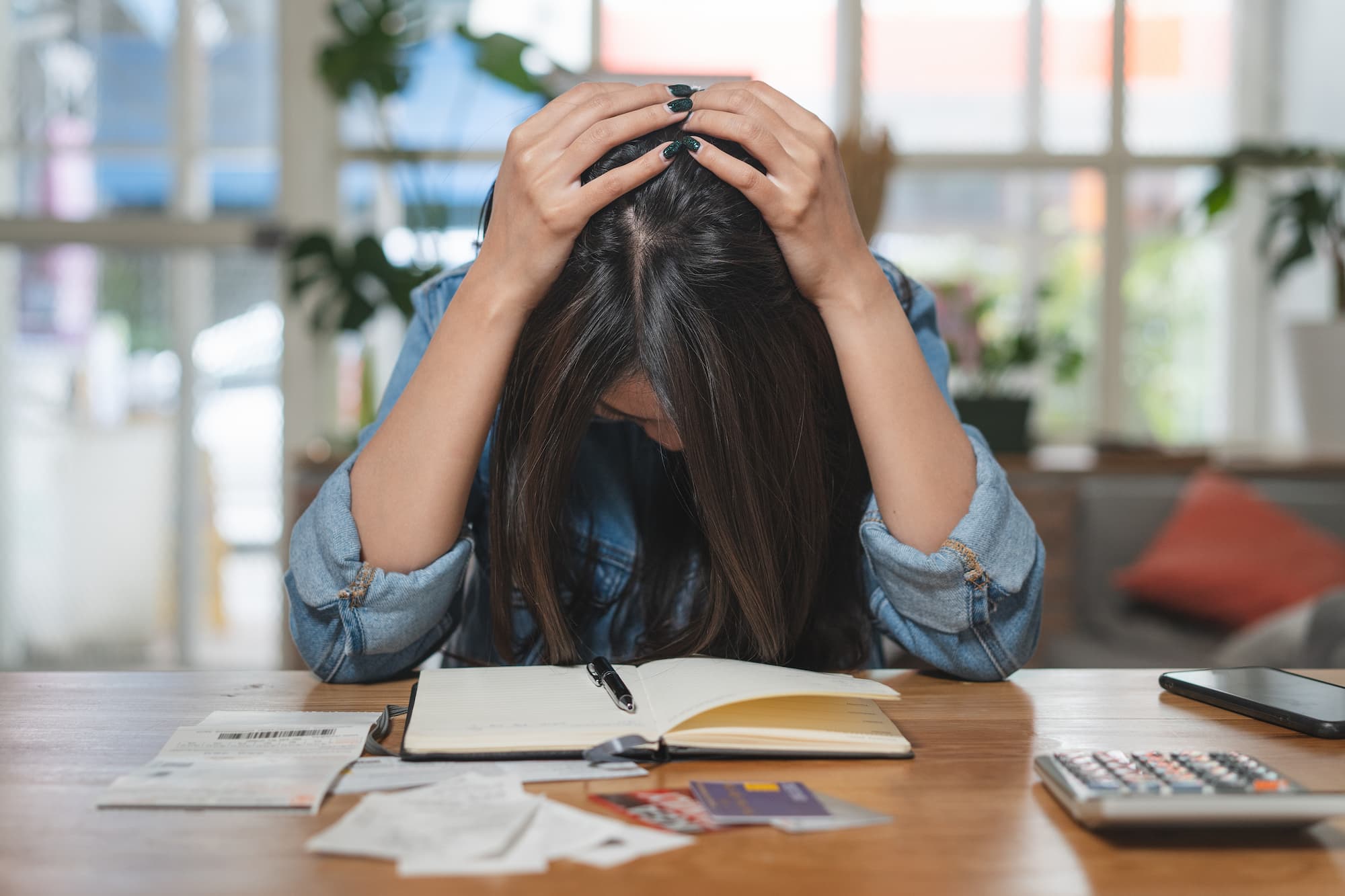 Jeune femme stressée tenant sa tête en regardant des papiers et un ordinateur portable sur une table en bois dans un environnement lumineux