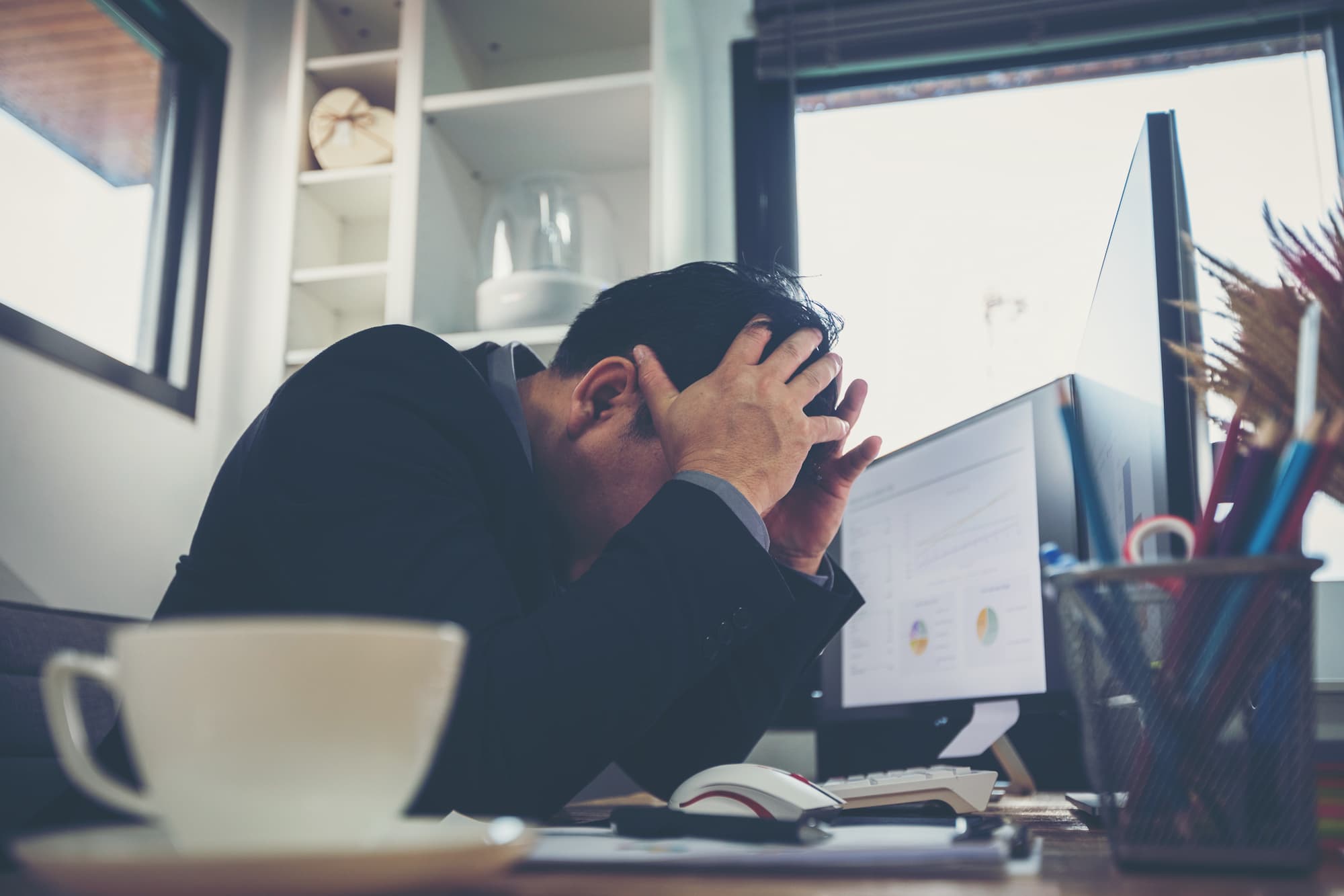 Homme d'affaires désespéré avec les mains sur la tête assis à son bureau avec un écran d'ordinateur montrant des graphiques de données