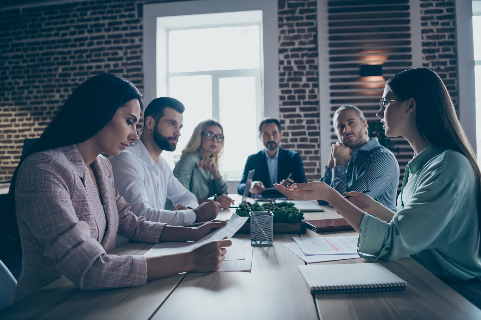 Réunion d'équipe diversifiée en discussion animée autour d'une table de conférence dans un bureau moderne avec des briques apparentes