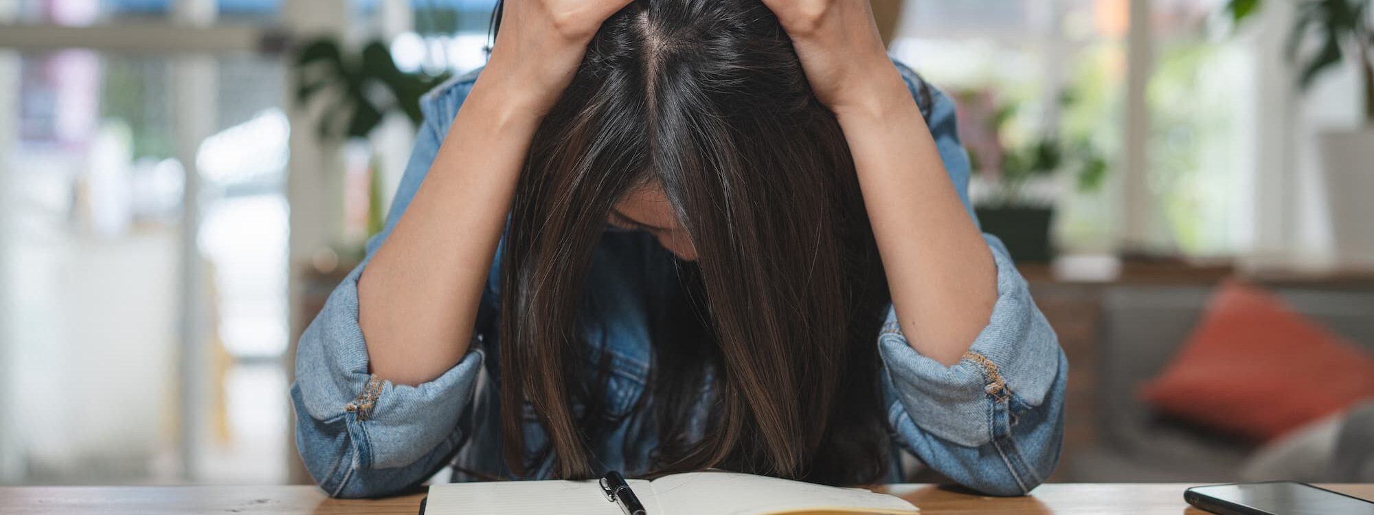 Jeune femme stressée tenant sa tête en regardant des papiers et un ordinateur portable sur une table en bois dans un environnement lumineux