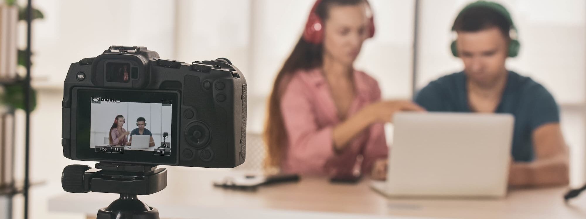 Deux personnes collaborant et filmées par une caméra sur un trépied, avec des écouteurs et un ordinateur portable.